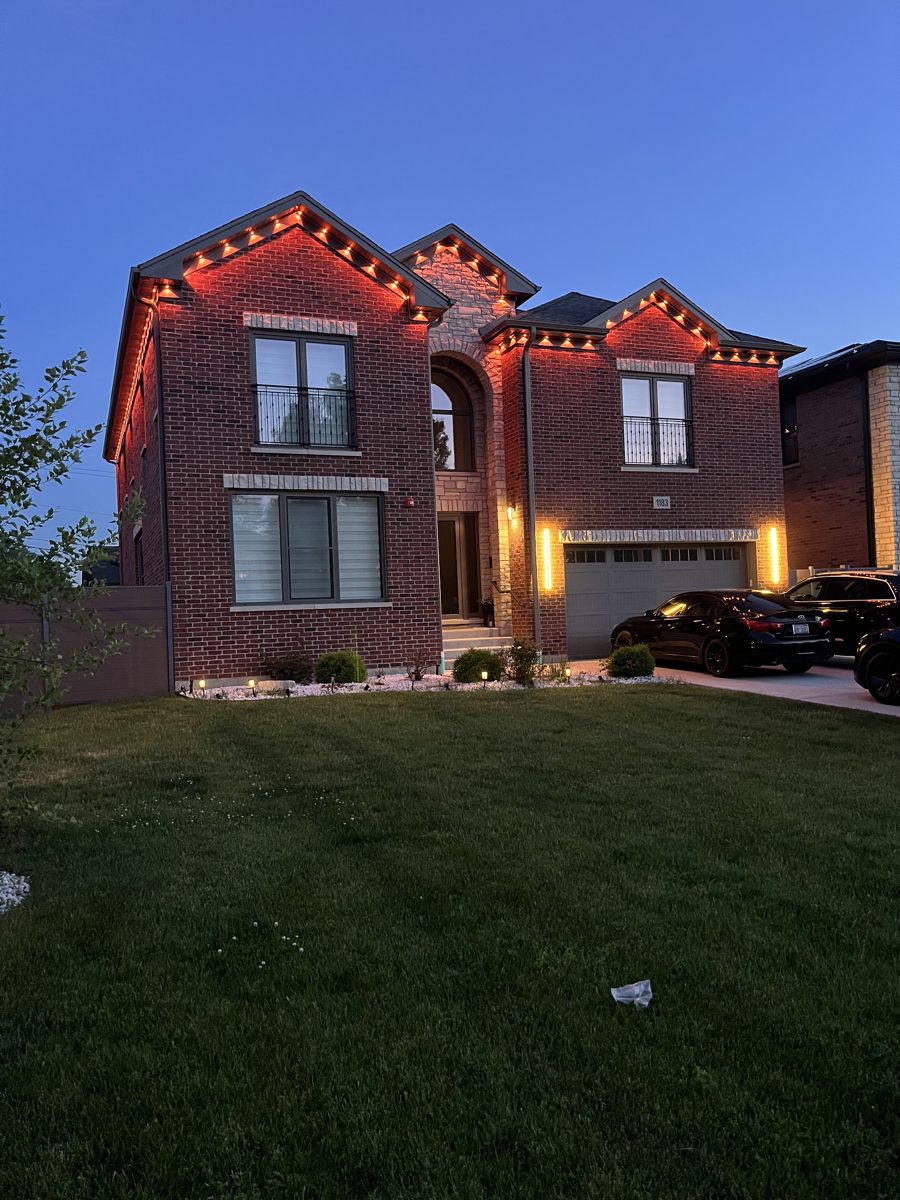 Two-story brick home with warm permanent lighting at dusk